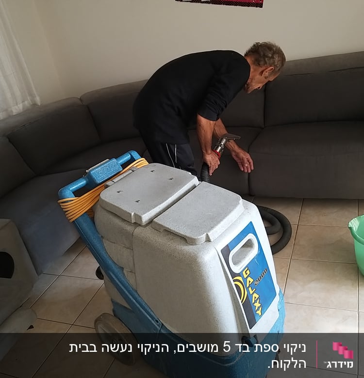 אדם מנקה ספה עם מכונת ניקוי מקצועית ודלי ירוק